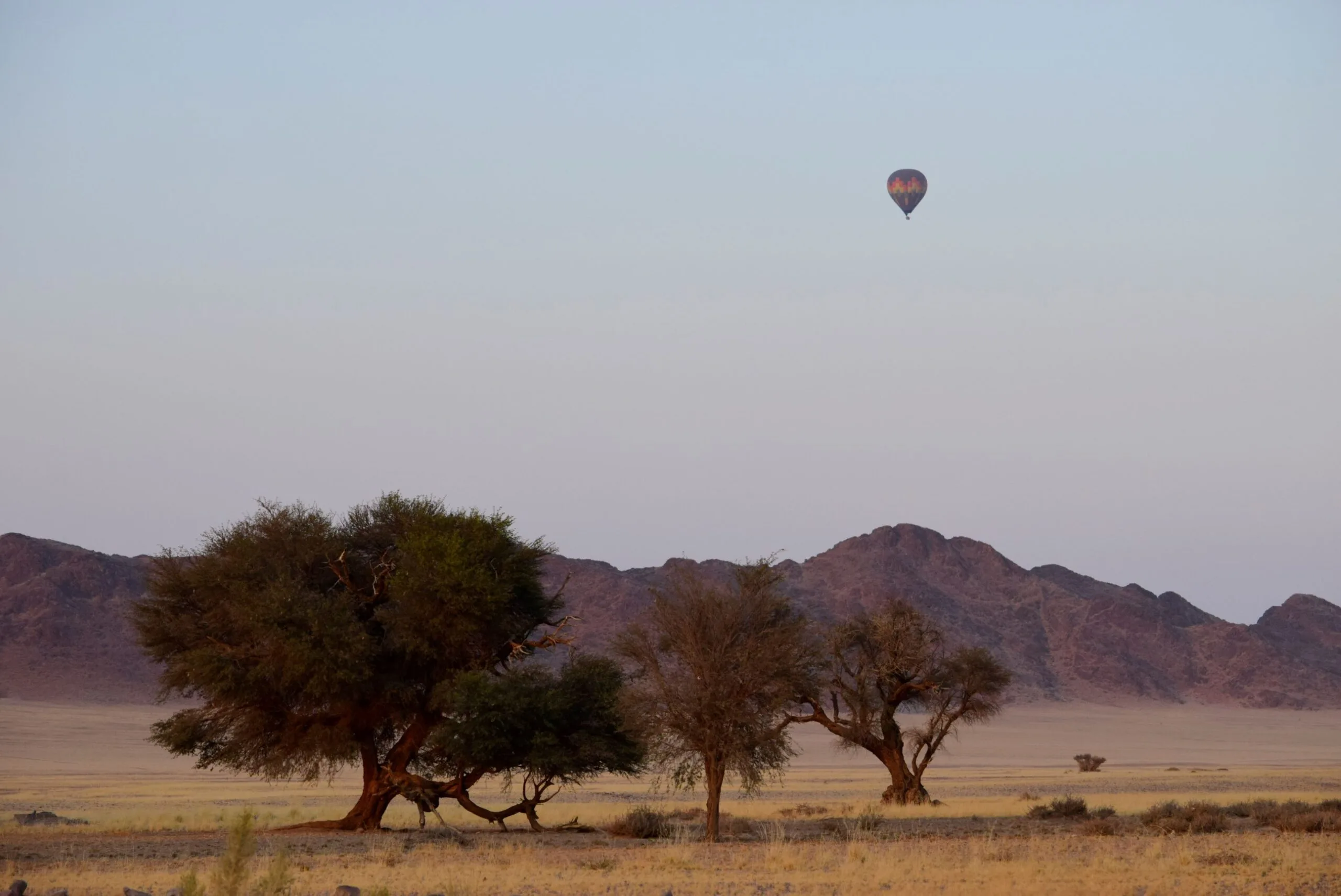 Balloon drifting over open savannah with a distant mountain range on the horizon