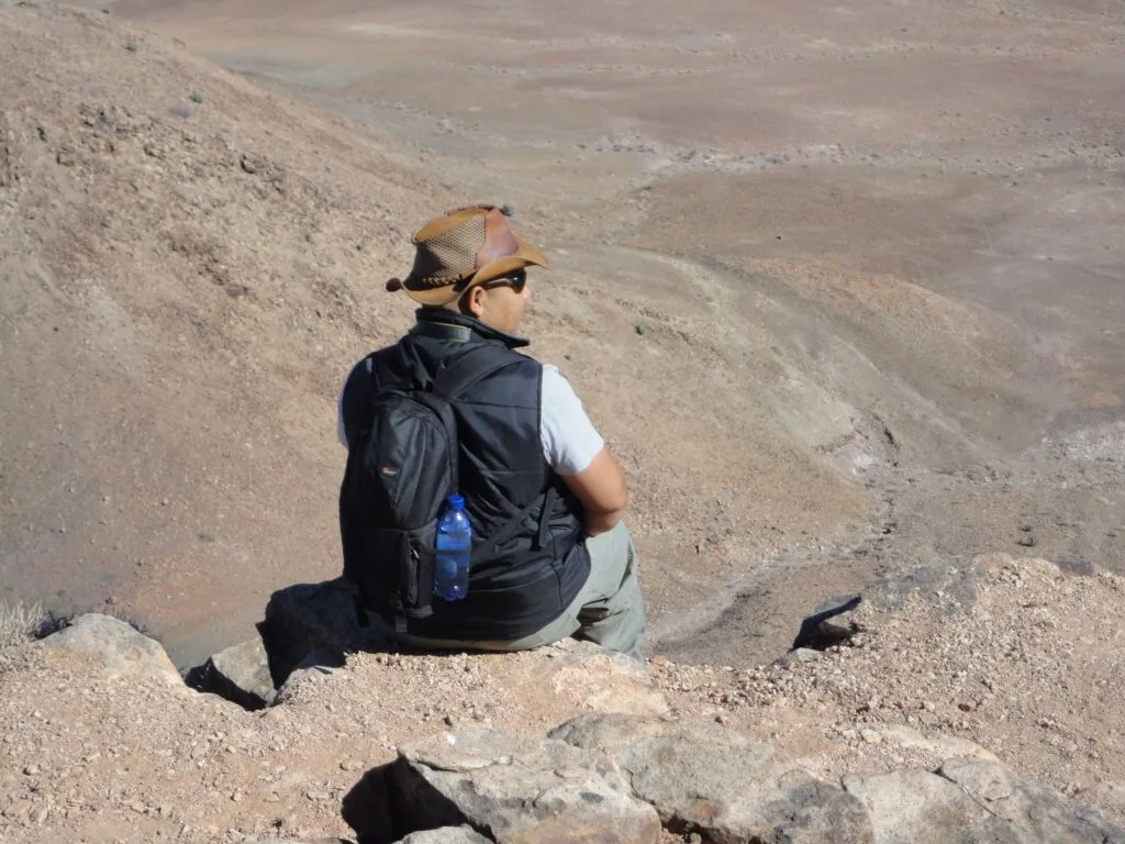 Francis McKay perched on a mountain top gazing into a canyon, back to camera