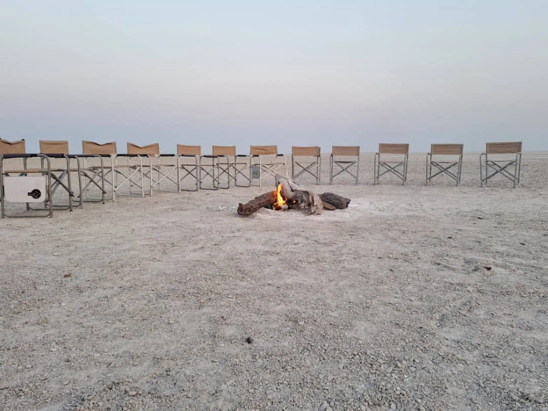 Camp chairs arranged in a circle around a newly lit bonfire on the flat Kgalagadi salt pan