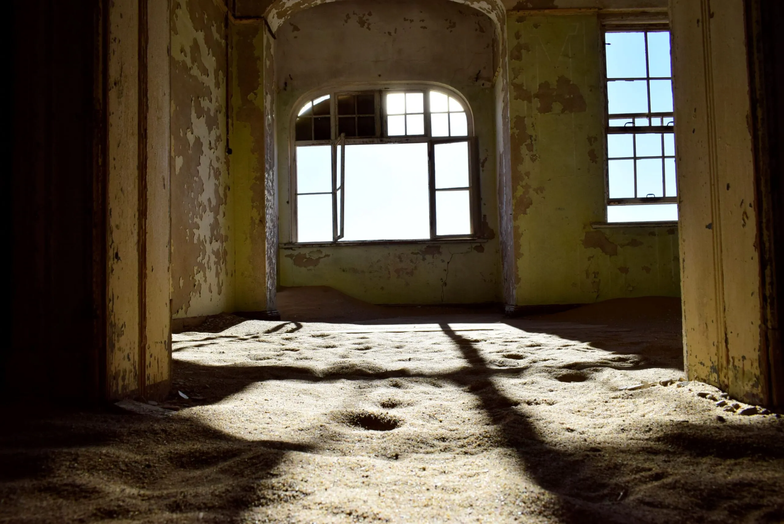 Looking out through a glassless window of a sand-filled Kolmanskop house, peeling green paint on the walls