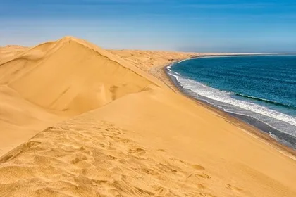 View from the top of a small dune where the Namib sand meets the Atlantic Ocean under a blue sky