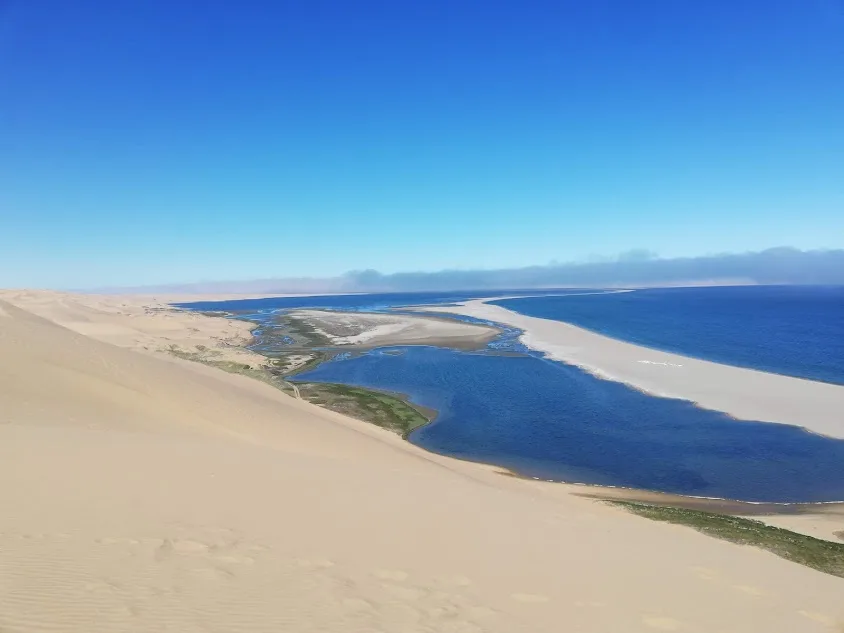 View from a dune vantage point over the body of water dammed by dunes at Sandwich Harbour, with river channels and distant water beyond