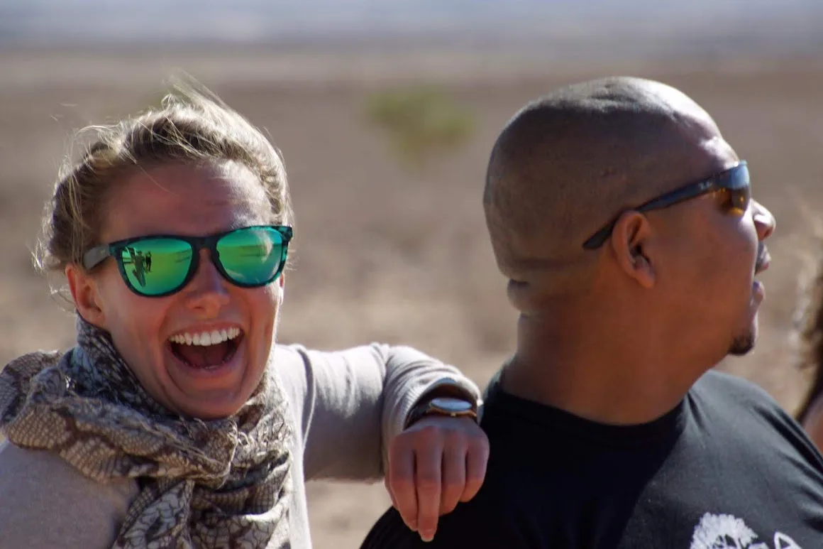 A tourist laughing out loud in green reflective sunglasses, arm around Francis McKay